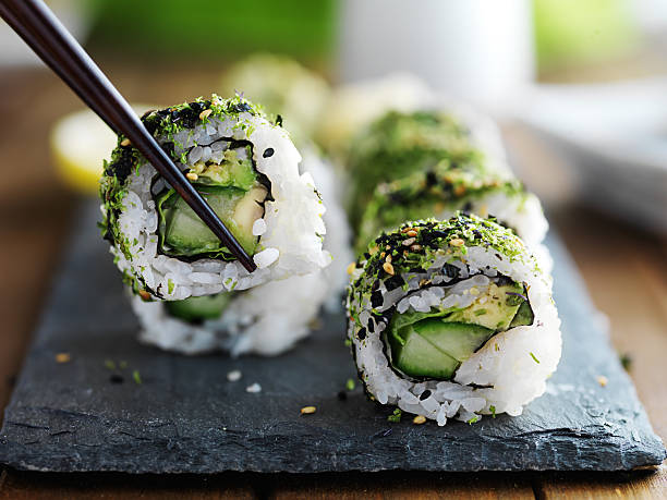 eating healthy kale sushi eating healthy kale and avocado sushi roll with chopsticks japanese cuisine food rolled up japanese culture stock pictures, royalty-free photos & images