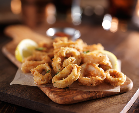 fried calimari rings on wooden tray with dipping sauce shot with selective focus