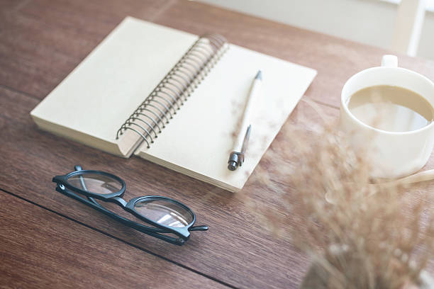 istock Notebook and cup of coffee with sunlight on desk office 593299516