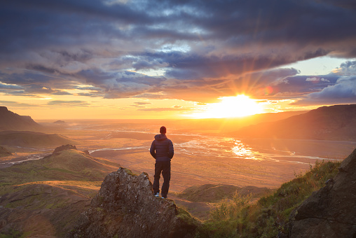 Man standing on a ledge of a mountain, enjoying the sunset over a river valley in Thorsmork, Iceland. 
