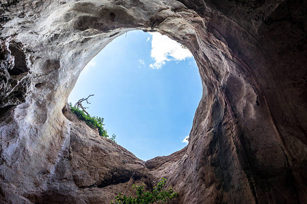 istock Large hole in rocky cave with blue sky 593308110