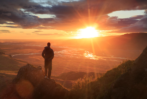 Man standing on a ledge of a mountain, enjoying the sunset over a river valley in Thorsmork, Iceland. With lens flare.
