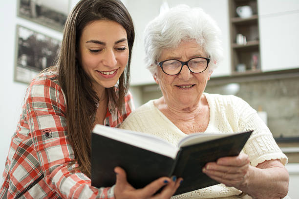 abuela y nieta leyendo libro juntos en casa. - care community 80 plus years cheerful fotografías e imágenes de stock
