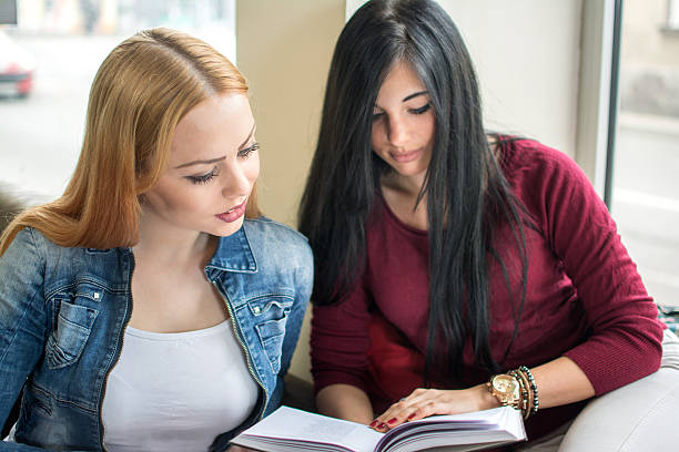 istock Two female friends reading book. 593318816