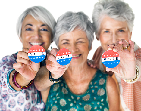 Studio portrait of a group of senior women holding up election buttons against a white background