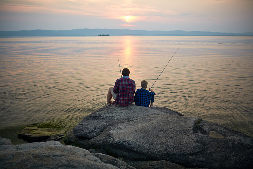 Two fishermen sitting on stone by lake in the evening