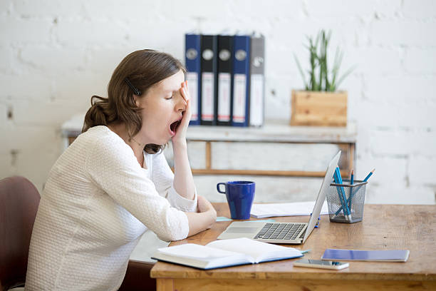 Sleepy young worker woman yawning Portrait of young woman sitting at table in front of laptop, sleepy, tired, overworked, lazy to work. Attractive business woman yawning in home office relaxing or bored after work on laptop computer checking the time photos stock pictures, royalty-free photos & images