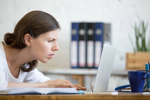 Young concerned office woman looking at laptop computer Young stressed businesswoman sitting with laptop and looking at screen with concerned facial expression. Surprised and focused business person staring at laptop computer screen worried and interested squint eyes stock pictures, royalty-free photos & images