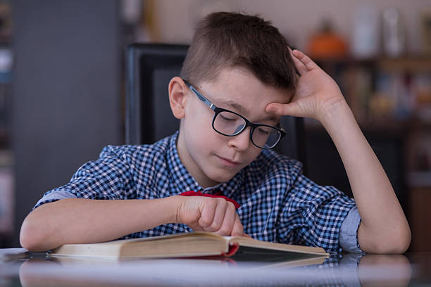 istock Cute school boy reading a book for homework 593330028