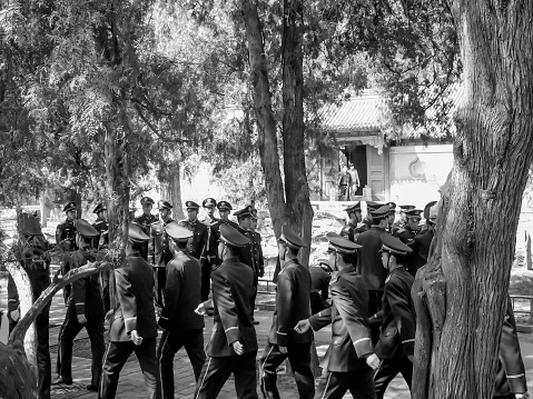 Beijing, China - March 31, 2007: Black and white image of groups of soldiers (in uniform) of the Chinese Army are standing together resting or marching under tall pine trees in the summer palace on a sunny day in spring.