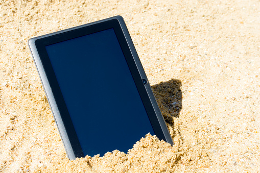 A tablet in sand on the beach.