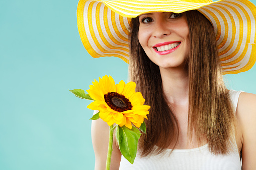 Portrait of attractive summer woman in yellow hat with sunflower in hand on blue background