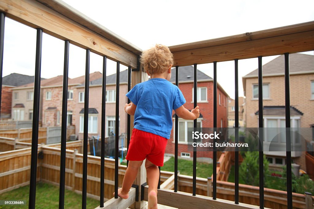 Little boy standing on the balcony Little boy standing on the balcony (patio) above the ground and trying to climb on balcony railing. House living and child-proofing  Balcony Stock Photo