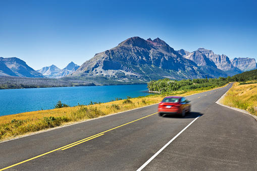 Glacier National Park, Montana, USA. A favorite tourist travel destination with mountain glacier and glacial lakes along the highway. Road trip visitors touring the park with their cars, travels the road for the scenic landscape. Horizontal format with copy space.