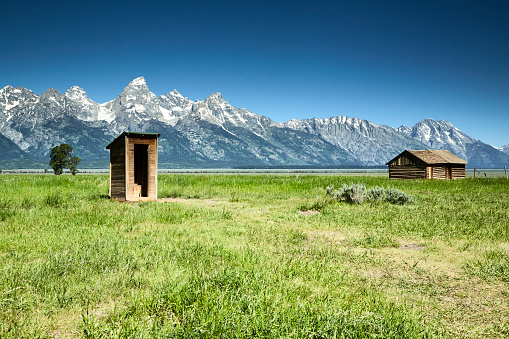 Wooden outhouse and barn are part of a series of structures in a historic settlement called Mormon Row. This settlement is near the base of the Grand Tetons.