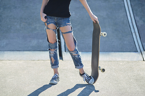 young woman holding a skateboard in torn jeans
