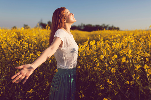 Beautiful smiling redhead enjoying a carefree summer day in a yellow flower field.