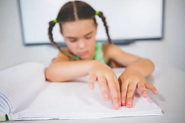 Schoolgirl reading a braille book in classroom at school
