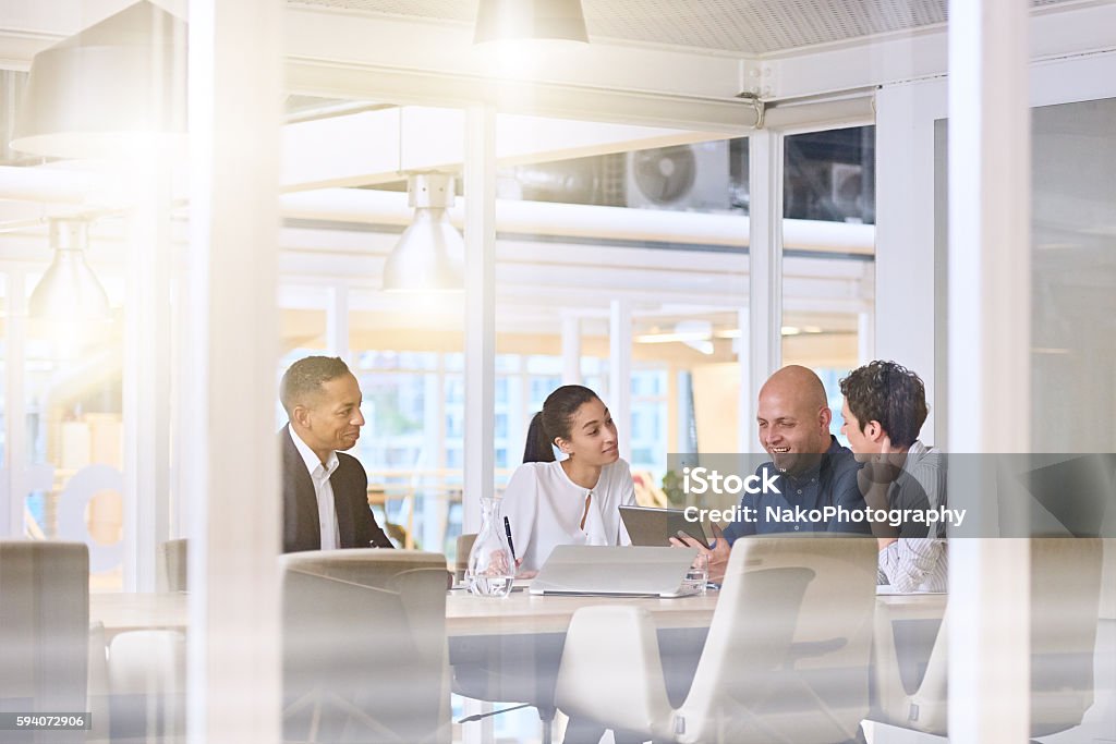 early morning sunrise business meeting in modern office conference room Corporate business meeting in modern office with glass walls, flare from the sunlight and reflections on the glass while business discussions take place amongst board members. Office Stock Photo