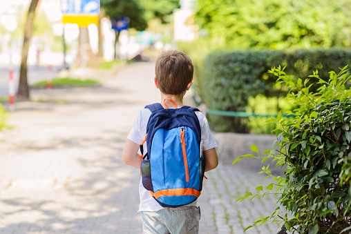 Little 7 years schoolboy going to school. Dressed in white t shirt and shorts. Blue backpack