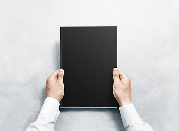 istock Hand holding black magazine with blank cover mockup. 594448644