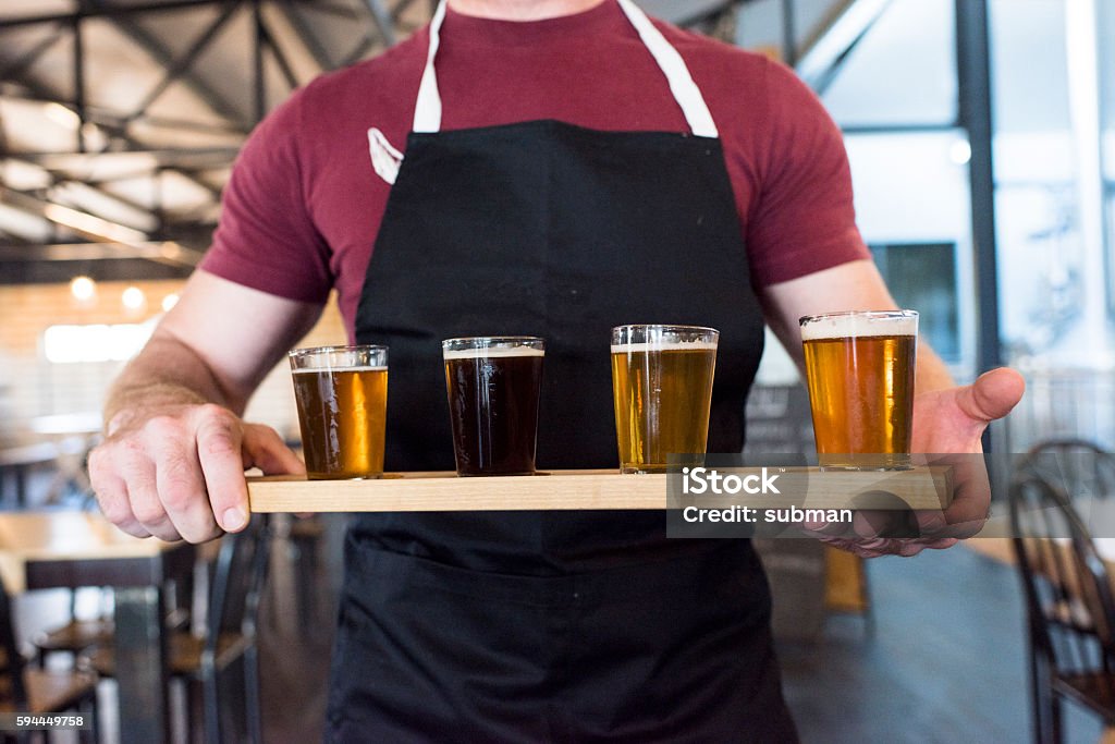 Waiter Holding A Tray Of Beer Tasting Glasses Male waiter holding a tray of filled beer tasting glasses inside a brewery. Exploration Stock Photo