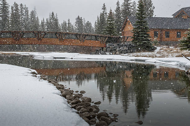 istock Falling Snow on Pedestrian Bridge, Log Building and Creek 594453494