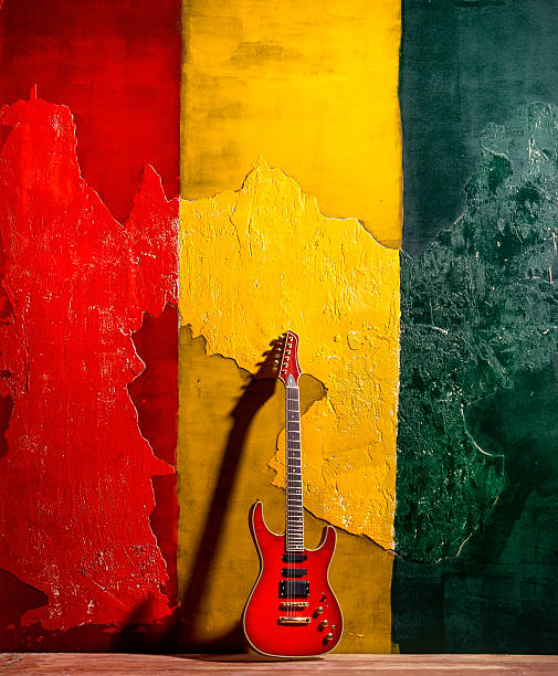 Kingston, Jamaica.- November 7, 2014:  a red guitar standing outside against a wall painted in the colours  red,yellow and green in the sun. The sun casting the guitar's shadow against the wall
