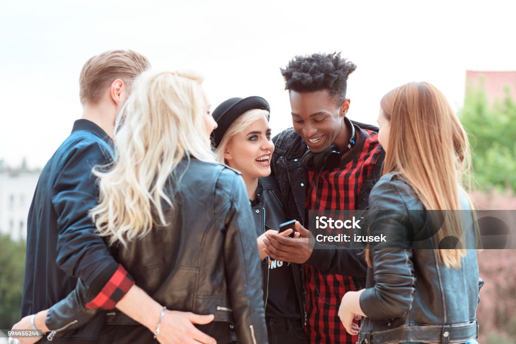 Multi ethnic group of friends using mobiles outdoors Multi ethnic group of happy young people using smart phone outdoors. Cool Attitude Stock Photo