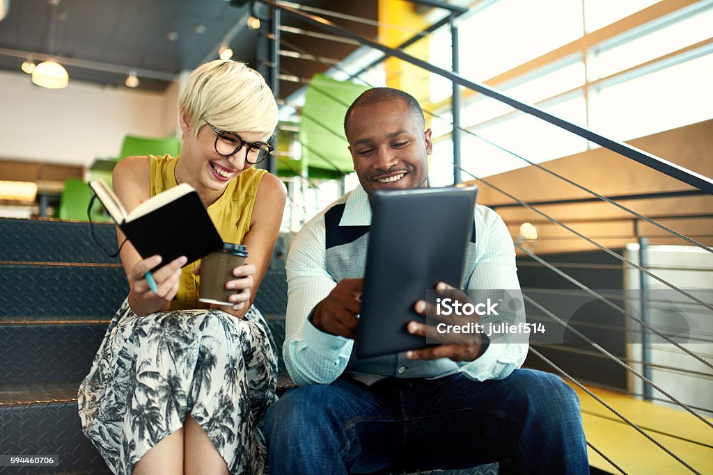 Two creative millenial small business owners working on social media Team of young casual business people collaborating on an online project using a digital touchpad tablet computer in a bright modern office space. Serie with light flares Office Stock Photo