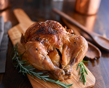 rotisserie chicken on wooden serving tray with herbs and rosemary