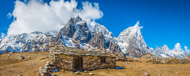 Simple Sherpa barn with stone roof overlooking high altitude summer yak pasture beneath the snowy Himalayan mountain peaks of the Everest National Park, Nepal.