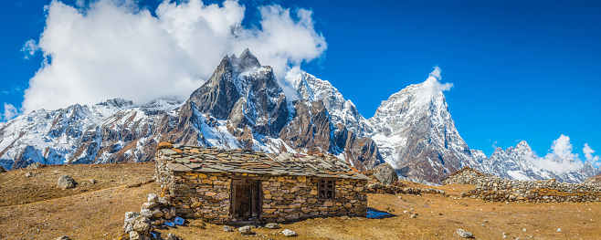 Simple Sherpa barn with stone roof overlooking high altitude summer yak pasture beneath the snowy Himalayan mountain peaks of the Everest National Park, Nepal.