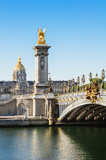 Alexandre III bridge and Hotel des Invalides in the background in the summer morning. Bridge decorated with ornate Art Nouveau lamps and sculptures.
