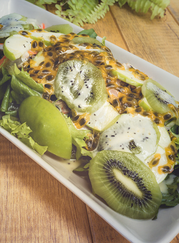 Mixed fresh salad leaves and fruit with passion fruit cream on wooden background. Healthy food.