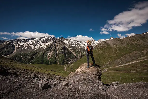Hiker with backpack standing on top of a mountain and enjoying valley view