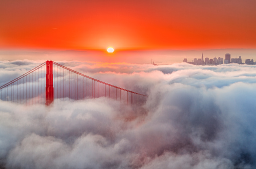 Early morning fog blankets the Golden Gate, sunrise red the sky.