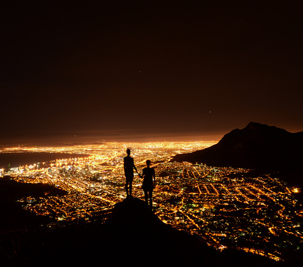 Two friend holding hand looking over the city lights of Cape Town from the top of the mountain - South Africa