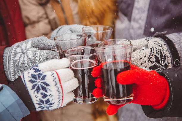 Cheers and happy holidays Close up of hands holding cups with hot wine. Friends cheering with glasses. Wearing warm knitted gloves. mulled wine photos stock pictures, royalty-free photos & images