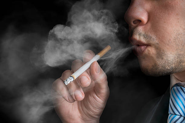 istock Young man holds cigarette and smoking. Low key photo. 594476358