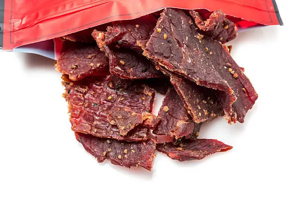 Beef Jerky close up coming out of it bag on white from above