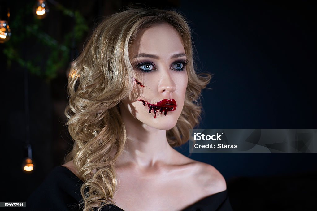 Woman with halloween make up and bloody face art Beautiful young blonde woman in black dress with halloween make up and bloody face art, close up portrait Adult Stock Photo