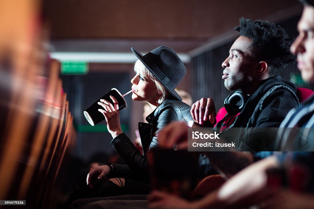 Multi ethnic young people in the movie theater Afro american young man and blonde woman watching movie in the cinema, woman drinking juice. Adult Stock Photo