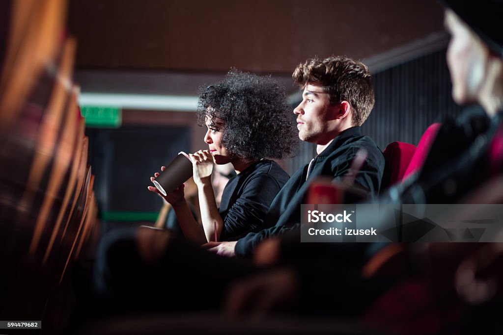 Young people in the movie theater Young people in the movie theater, afro woman drinking juice. Side view. Adult Stock Photo