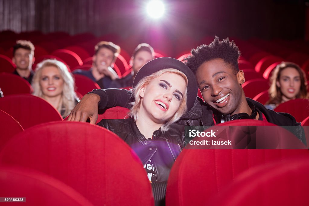 Multi ethnic couple in the movie theater Group of happy young people in the 3D movie theater, watching comedy. Focus on young couple - blonde girl and afro american guy. Hipster Culture Stock Photo