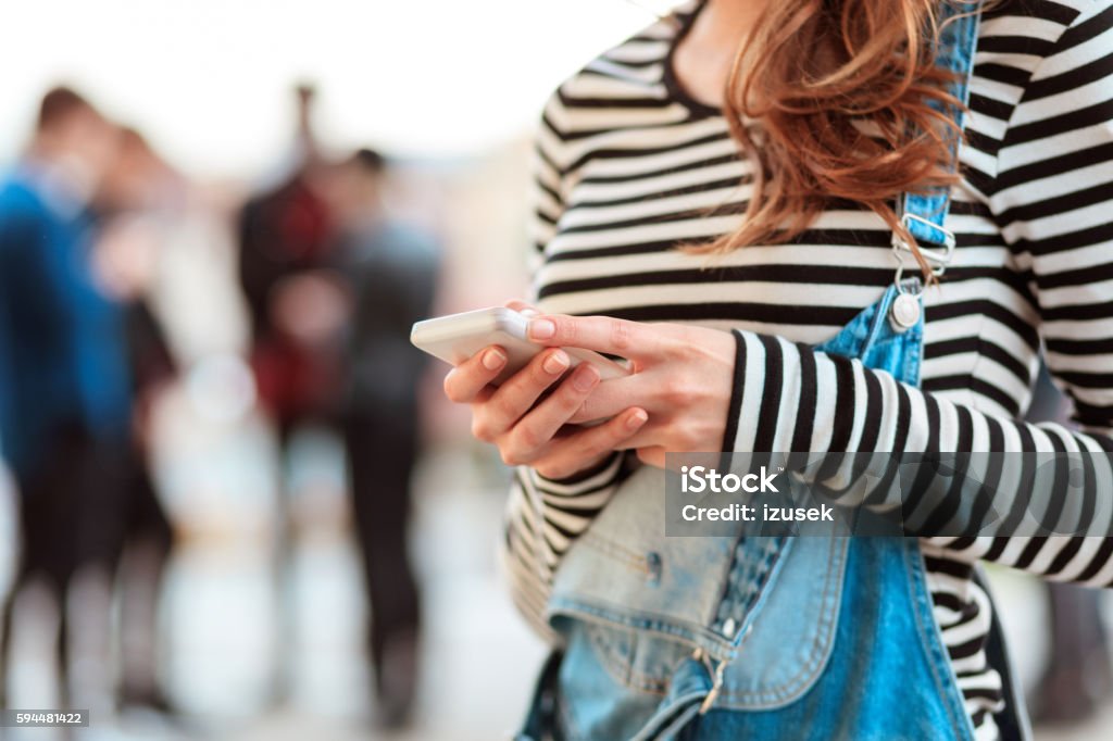 Young woman texting on smart phone outdoor Young woman texting on mobile outdoor. Defocused group of people in the background. 20-29 Years Stock Photo