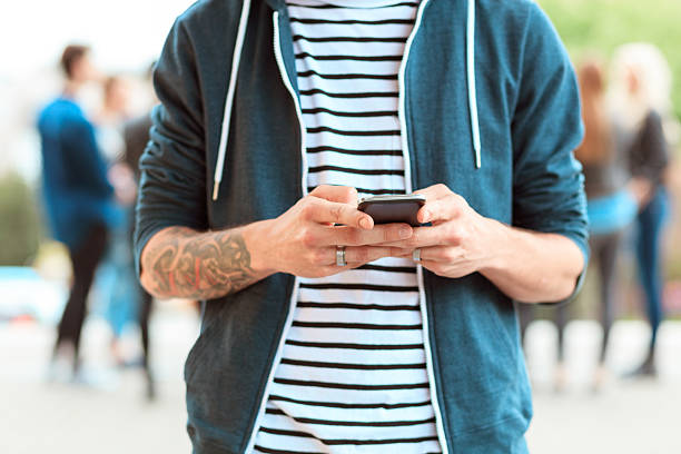 Young man texting on mobile outdoor. Group of people in the background.