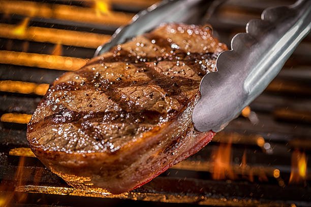 Grilling Filet Mignon Steak on a grill with Fire Grilling a filet mignon steak over open flame grill with tongs flipping the steak. Please see my portfolio for other food and drink images.  serving tongs stock pictures, royalty-free photos & images