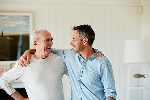 Smiling senior man with son standing arm around while looking at each other