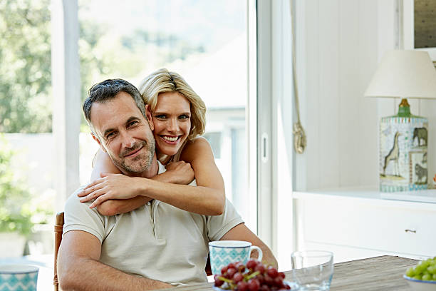 Smiling woman embracing man at home Portrait of smiling woman embracing man from behind at home cheek to cheek photos stock pictures, royalty-free photos & images
